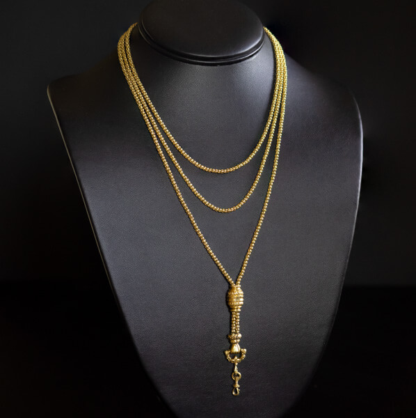 A long gold chain with a clasped hand decoration on a black neck form 